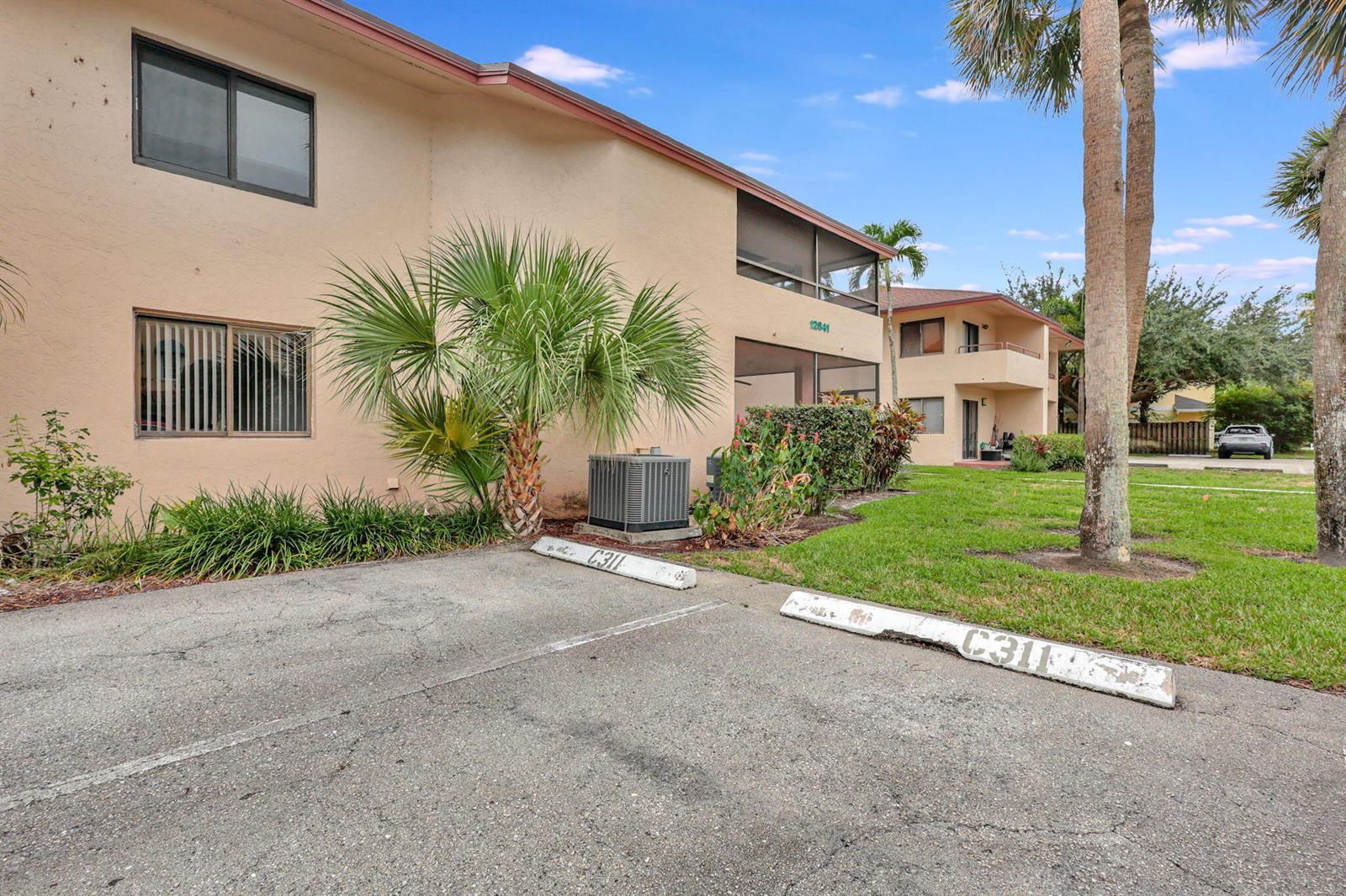 An exterior view of a multi-story apartment building with assigned parking spaces in the foreground — 12641 Westhampton Circle # C311, Wellington FL 33414, WELLINGTON, FL