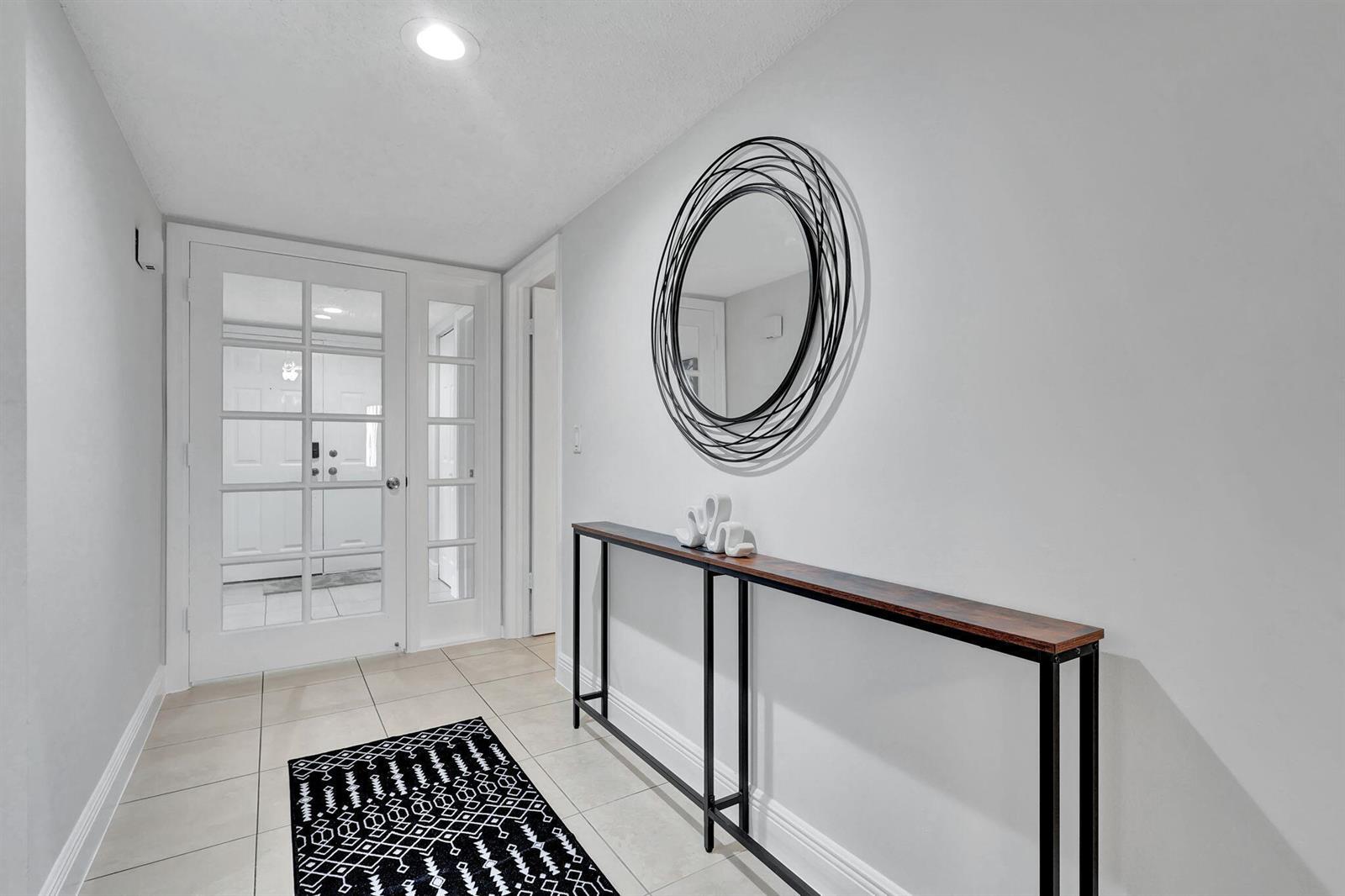 A bright entryway features a console table, a circular wall mirror, and a patterned rug — 12641 Westhampton Circle # C311, Wellington FL 33414, WELLINGTON, FL