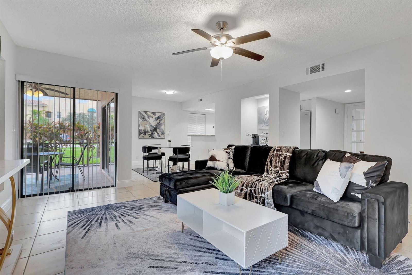A living room with a black sectional sofa, white coffee table, and sliding glass doors — 12641 Westhampton Circle # C311, Wellington FL 33414, WELLINGTON, FL