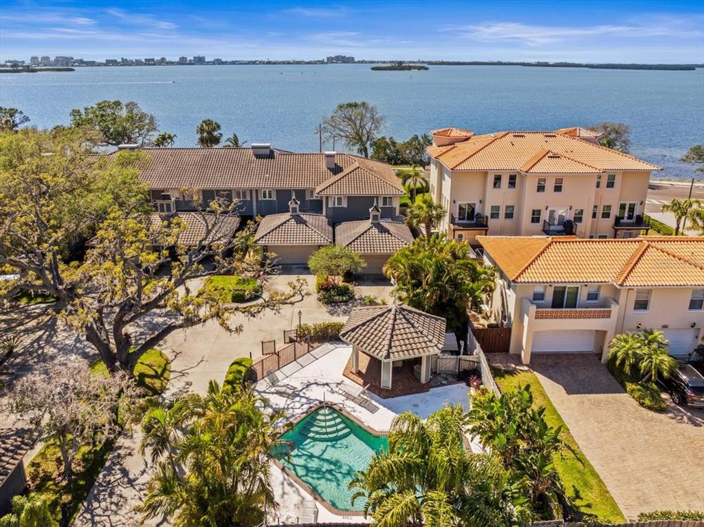 An aerial view shows a swimming pool, gazebo, and multi-story homes near a large body of water — 2087 EDGEWATER DRIVE UNIT C, CLEARWATER, FL