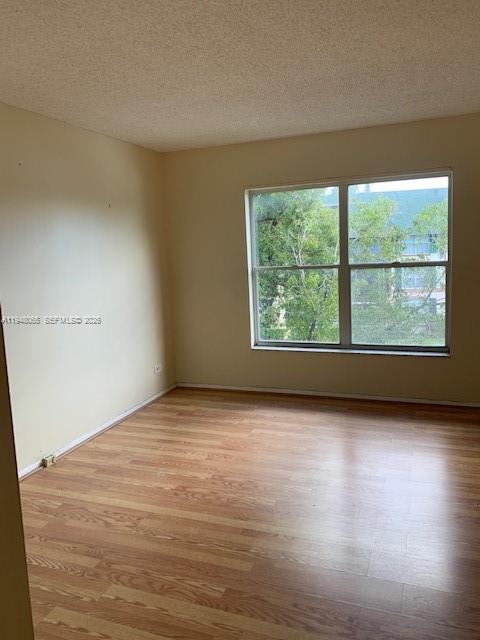 An empty room features light-colored walls, wood-look flooring, and a window overlooking trees — 3710 Inverrary Dr # 3K, Lauderhill FL 33319, LAUDERHILL, FL