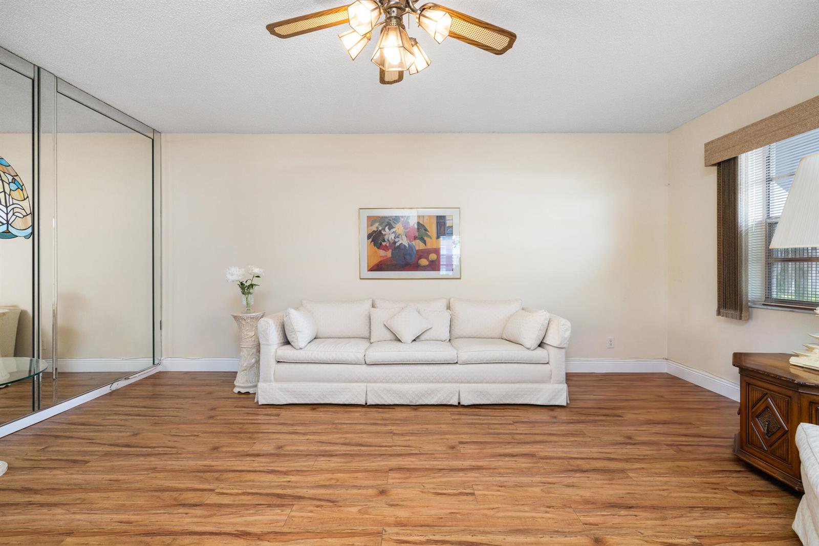 A living room features a white sofa, wood-look flooring, a ceiling fan, and mirrored closet doors — 97 Flanders # C, Delray Beach FL 33484, DELRAY BEACH, FL