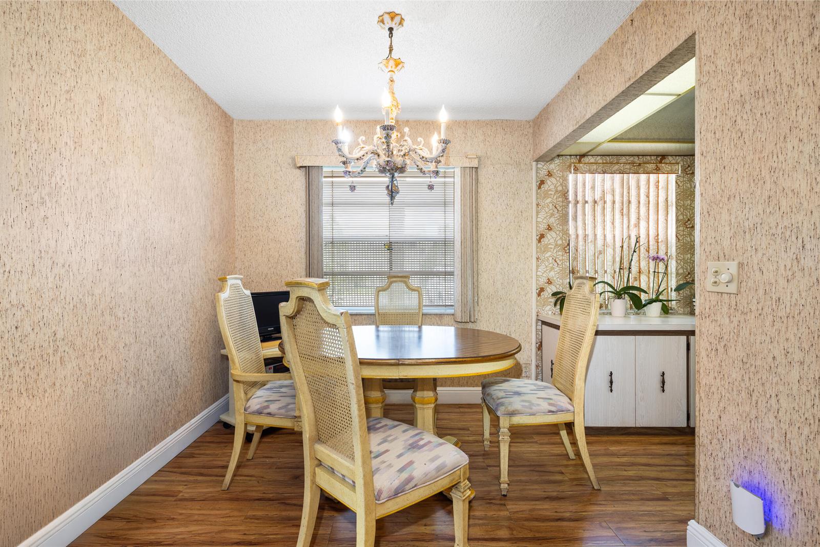 A dining room features a round wooden table, four cane-back chairs, and a crystal chandelier — 97 Flanders # C, Delray Beach FL 33484, DELRAY BEACH, FL