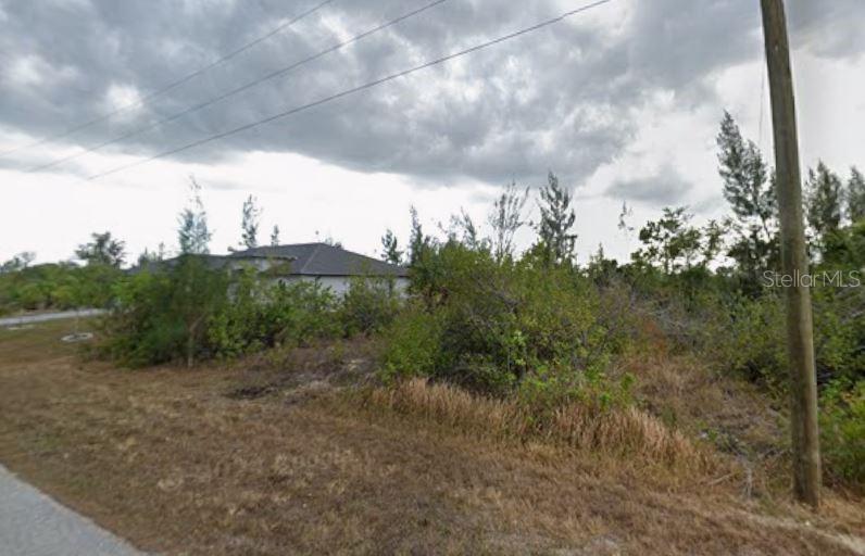 A vacant, overgrown lot with a utility pole and a neighboring house in the background — 9417 SUNDANCE STREET, PORT CHARLOTTE, FL