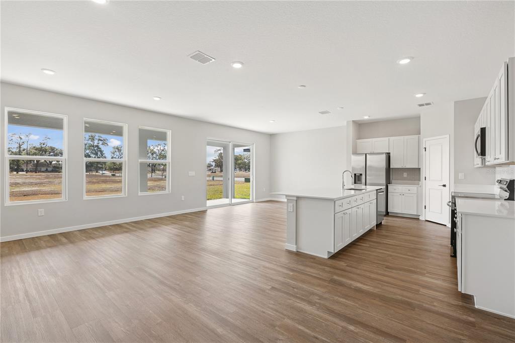 An open-concept kitchen and living area featuring white cabinetry, a central island, and wood flooring — 4480 NW 37TH STREET ROAD, OCALA, FL