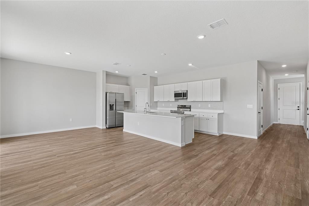 An open-concept kitchen features white cabinetry, stainless steel appliances, a center island, and wood-look flooring — 4480 NW 37TH STREET ROAD, OCALA, FL