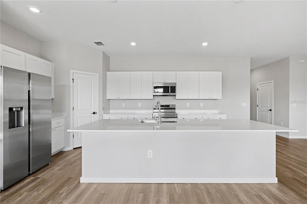 A modern kitchen features white cabinetry, stainless steel appliances, and a large central island — 4480 NW 37TH STREET ROAD, OCALA, FL