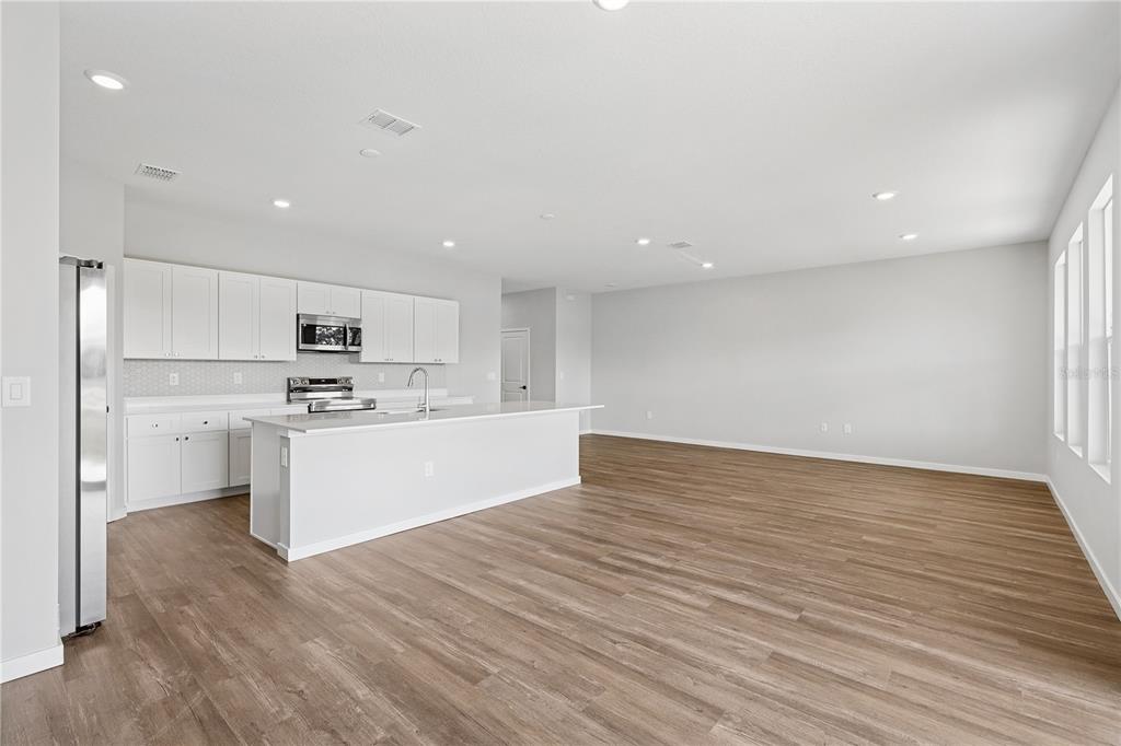 A modern kitchen with white cabinetry and a large island opens into a spacious living area — 4480 NW 37TH STREET ROAD, OCALA, FL