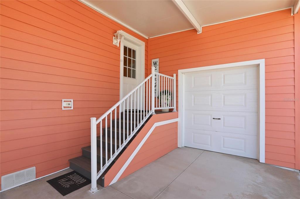 An exterior view showing a covered porch with orange siding, stairs, and a garage door — 24717 SNOOK AVENUE UNIT 11D, PUNTA GORDA, FL