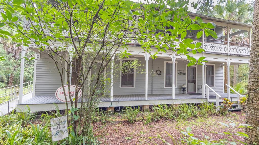 A two-story gray historic house features a wide wrap-around porch with white decorative railings — 200 PARK STREET, MELROSE, FL