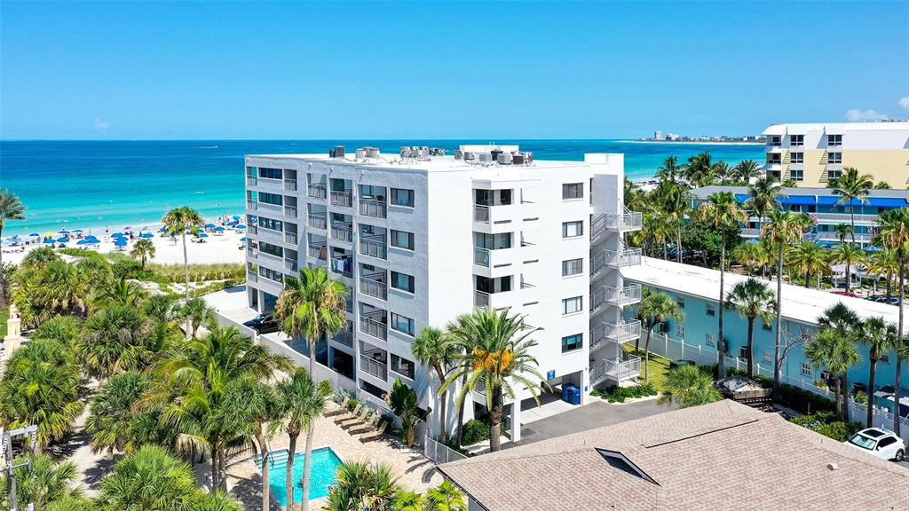 An exterior view of a multi-story white apartment building near a beach with palm trees — 1001 POINT OF ROCKS ROAD UNIT 208, SARASOTA, FL