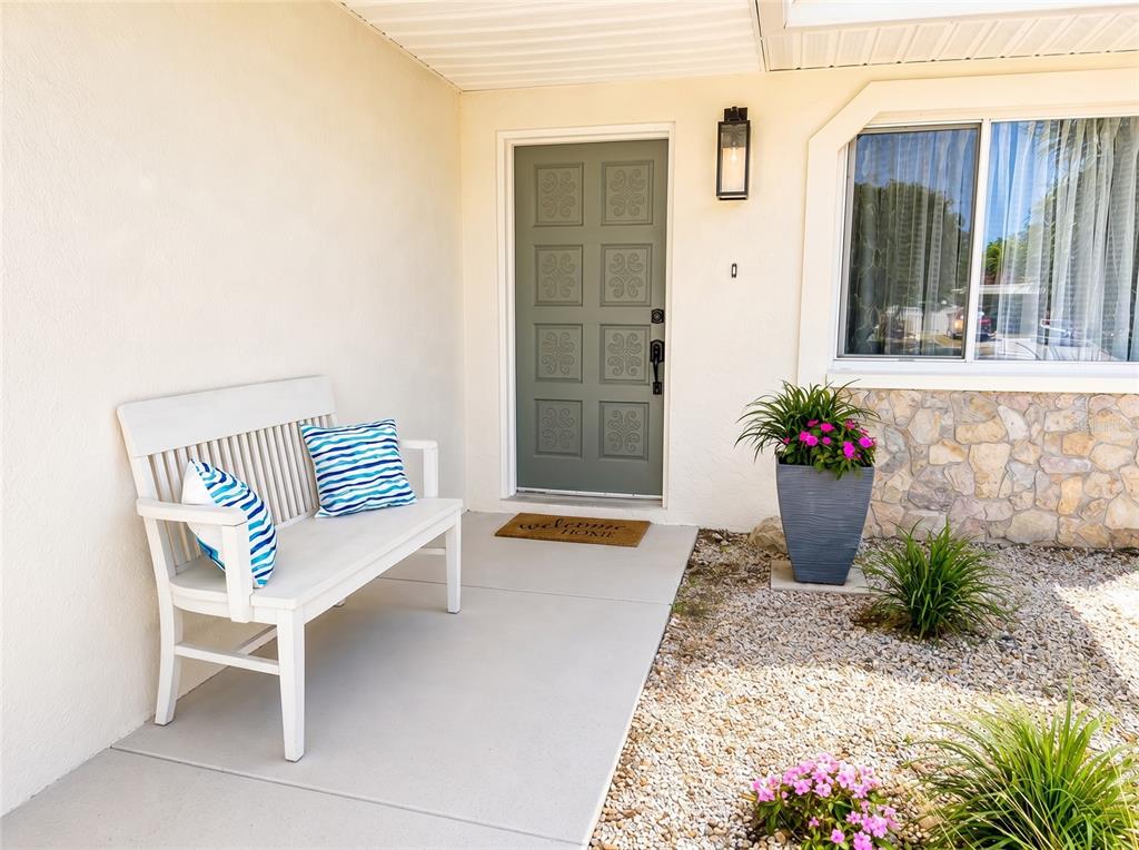 A white bench sits on a concrete porch next to a green door and stone siding — 7210 8TH AVENUE LOOP W, BRADENTON, FL