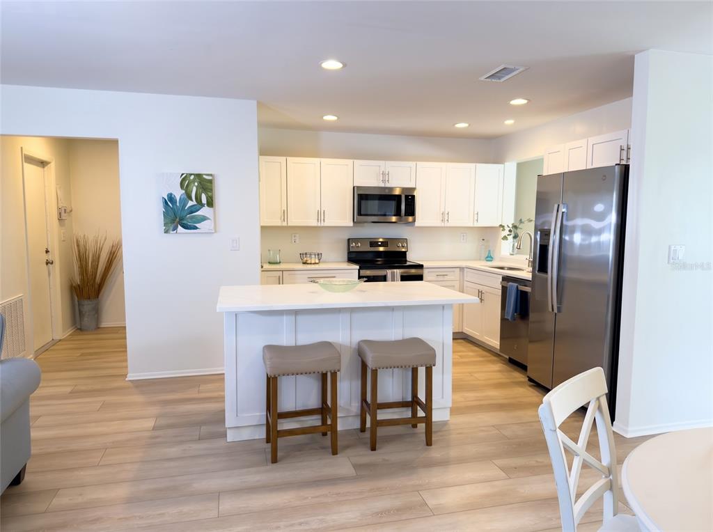 A kitchen features white cabinets, a central island with two stools, and stainless steel appliances — 7210 8TH AVENUE LOOP W, BRADENTON, FL
