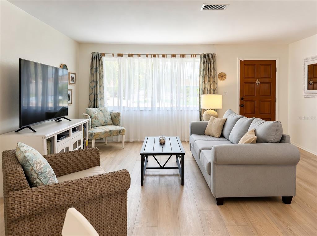 A living room features light wood flooring, a gray sofa, a coffee table, and a television — 7210 8TH AVENUE LOOP W, BRADENTON, FL