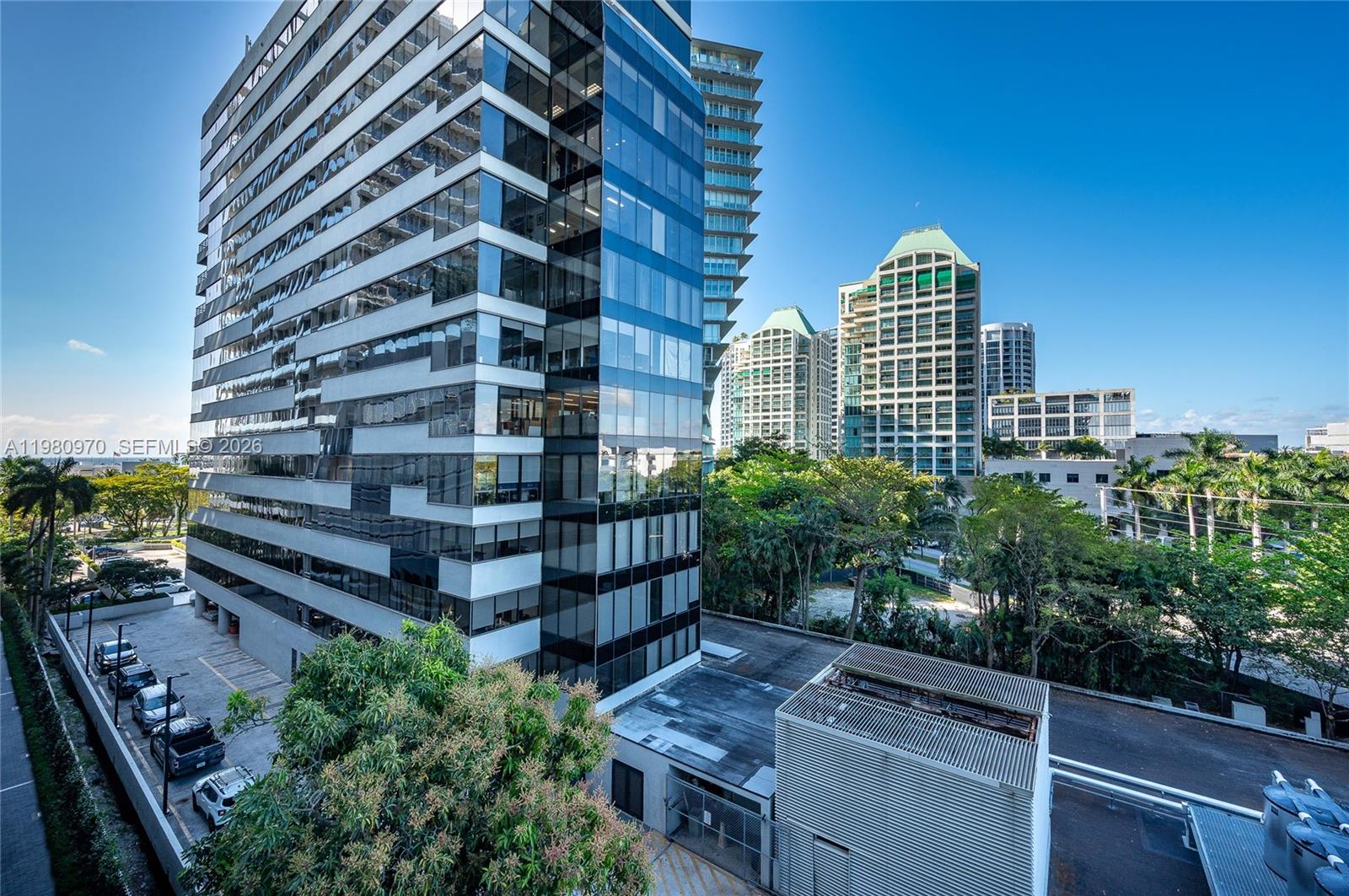 An exterior view of a modern glass office building with a parking lot below — 2678 Tigertail Ave # 413, Miami FL 33133, MIAMI, FL