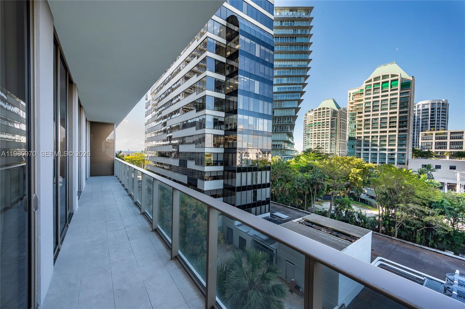 A balcony with a glass railing overlooks a city street and several modern high-rise buildings — 2678 Tigertail Ave # 413, Miami FL 33133, MIAMI, FL