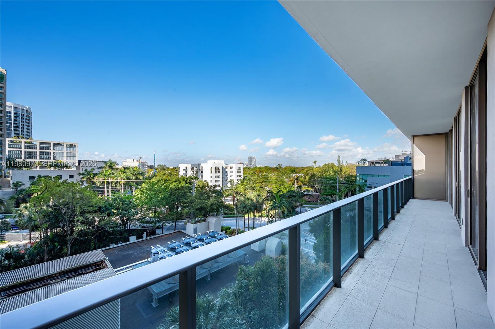 A balcony with a glass railing overlooks a city street, trees, and nearby buildings — 2678 Tigertail Ave # 413, Miami FL 33133, MIAMI, FL