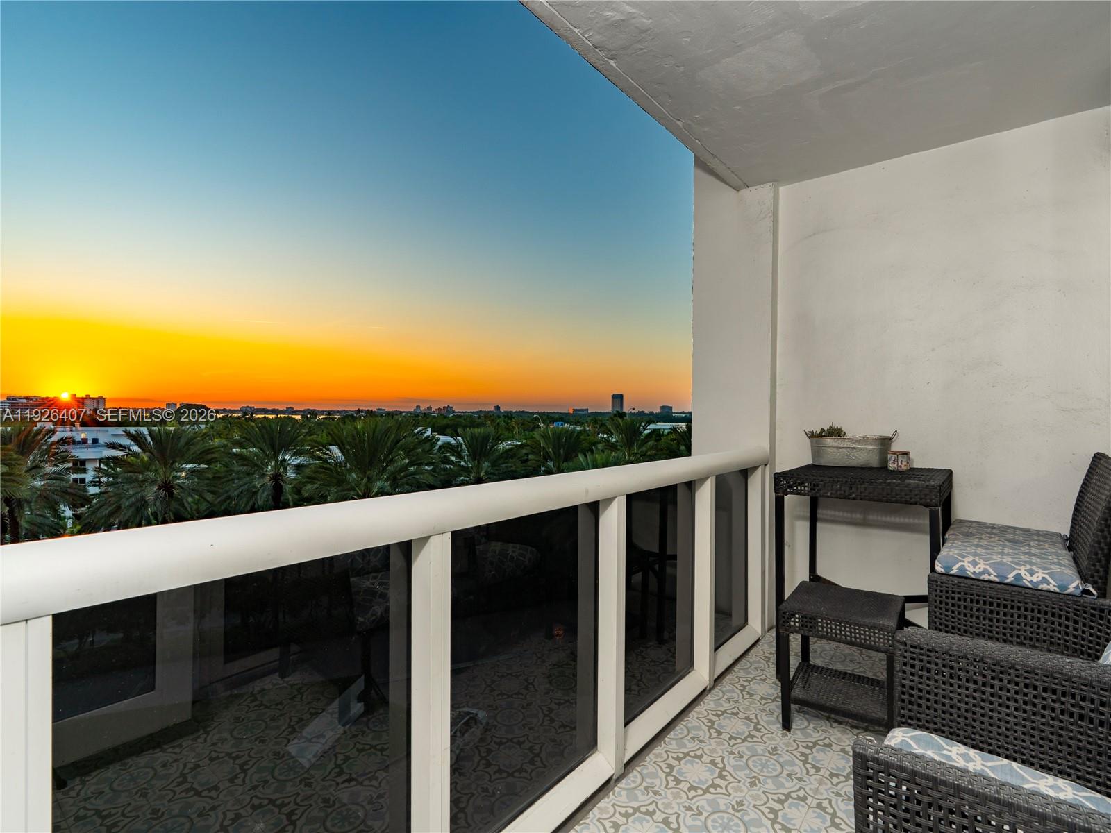 A balcony with patterned tile flooring, wicker furniture, and a sunset view over palm trees — 10275 Collins Ave # 527, Bal Harbour FL 33154, BAL HARBOUR, FL