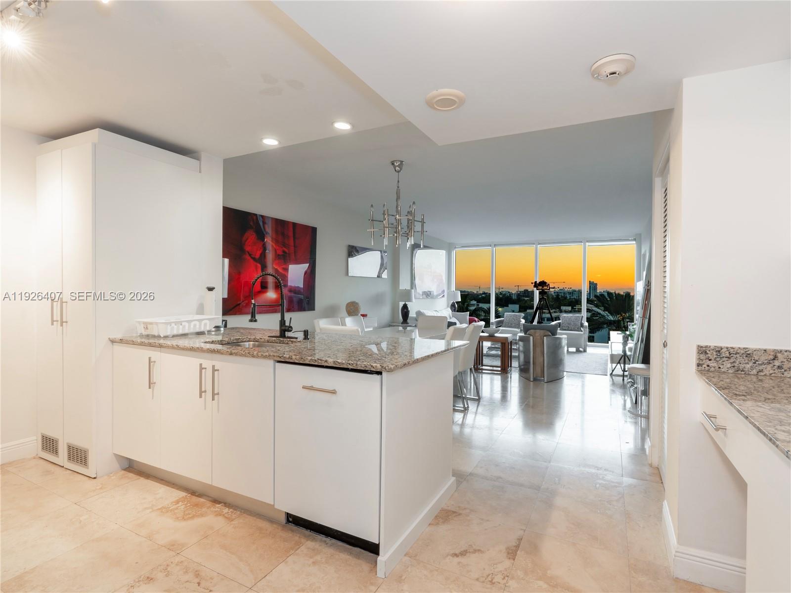 A kitchen with white cabinets and granite countertops overlooks an open living area with sunset views — 10275 Collins Ave # 527, Bal Harbour FL 33154, BAL HARBOUR, FL