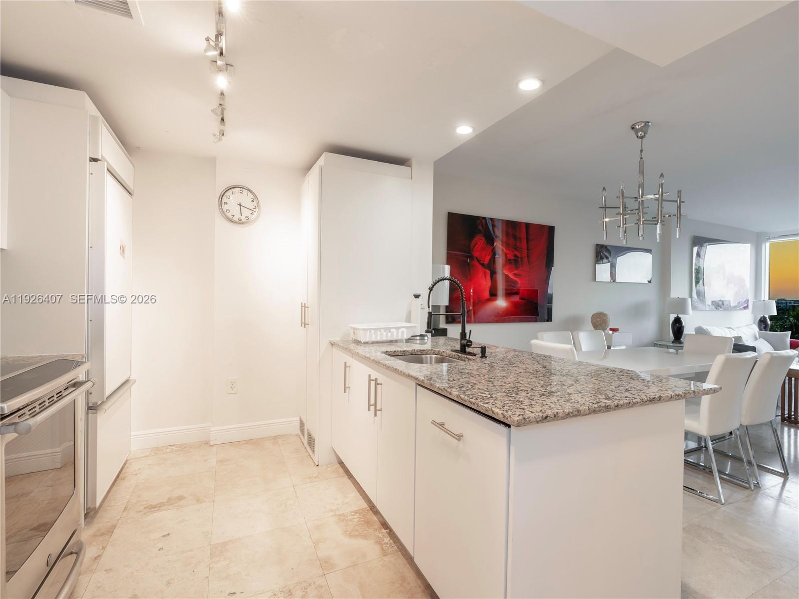 A kitchen with white cabinets, granite countertops, and a sink opens into a dining area — 10275 Collins Ave # 527, Bal Harbour FL 33154, BAL HARBOUR, FL