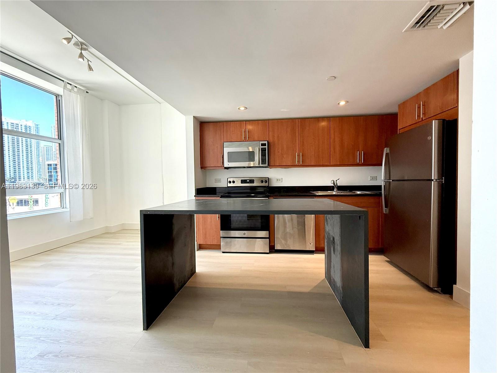A kitchen features wood cabinets, stainless steel appliances, and a black waterfall island — 111 E Flagler St # 805, Miami FL 33131, MIAMI, FL
