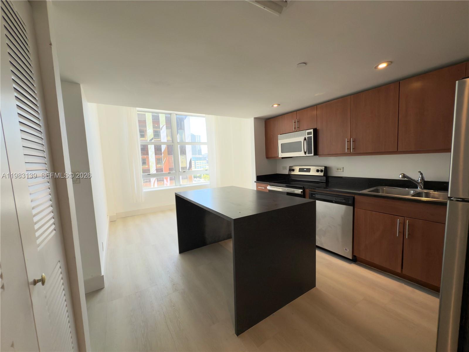 A kitchen features wood cabinets, black countertops, a central island, and light-colored flooring — 111 E Flagler St # 805, Miami FL 33131, MIAMI, FL