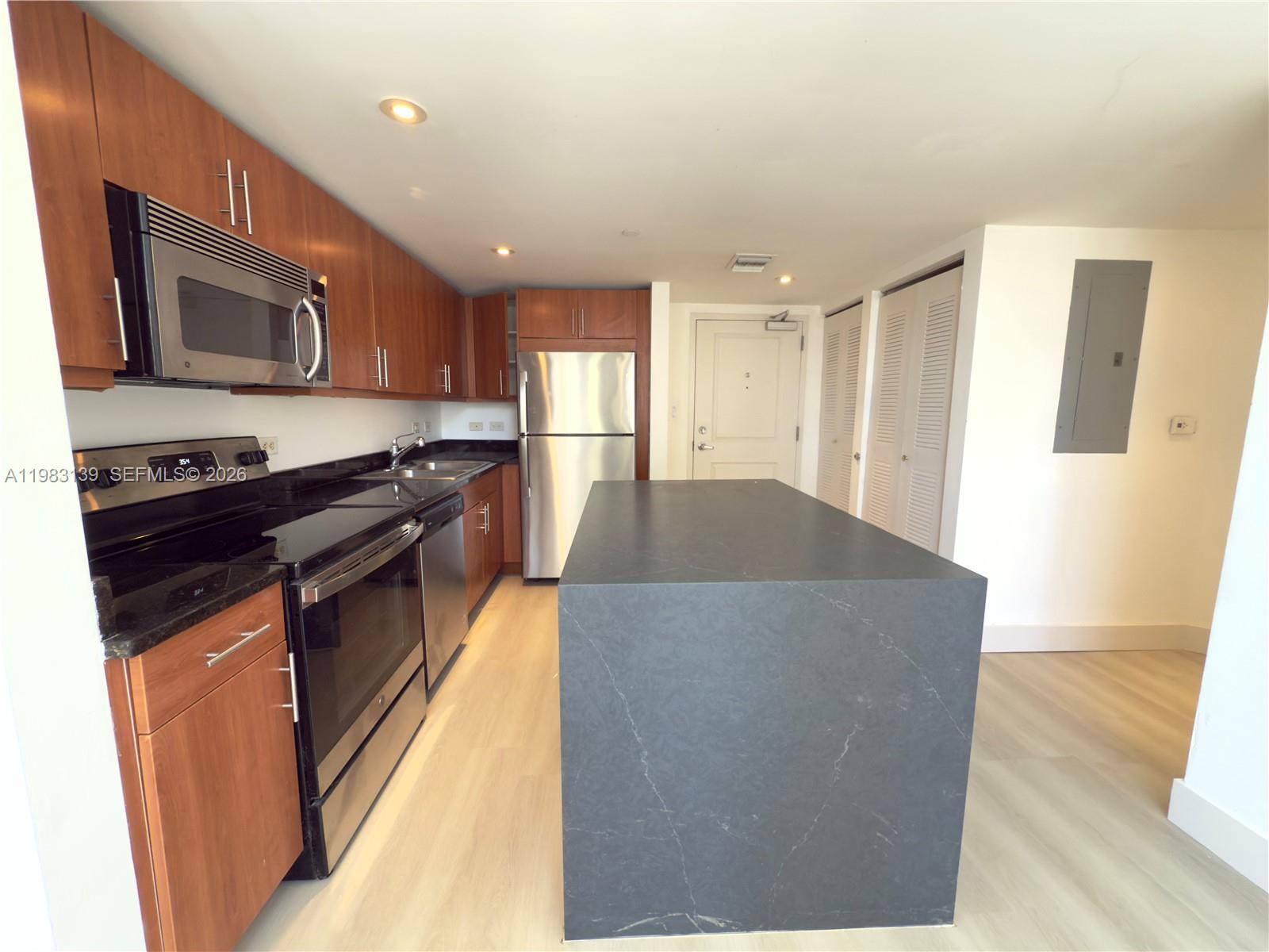 A kitchen features wood cabinets, stainless steel appliances, black countertops, and a large central island — 111 E Flagler St # 805, Miami FL 33131, MIAMI, FL