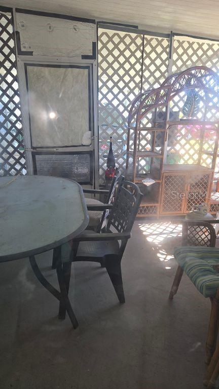 A screened-in porch features a glass-top table, dark plastic chairs, and a wicker shelving unit — 1398 IBIS DRIVE, ENGLEWOOD, FL