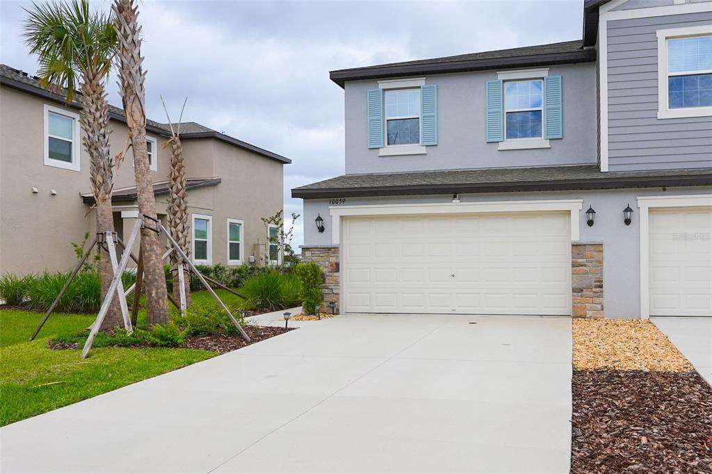 A two-story suburban home features a concrete driveway, a two-car garage, and light blue shutters — 10059 TRUMPET HONEYSUCKLE WAY, SAN ANTONIO, FL