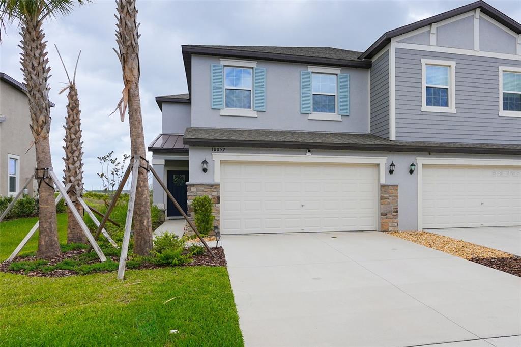 A two-story townhouse with a gray exterior, blue shutters, and a two-car garage — 10059 TRUMPET HONEYSUCKLE WAY, SAN ANTONIO, FL