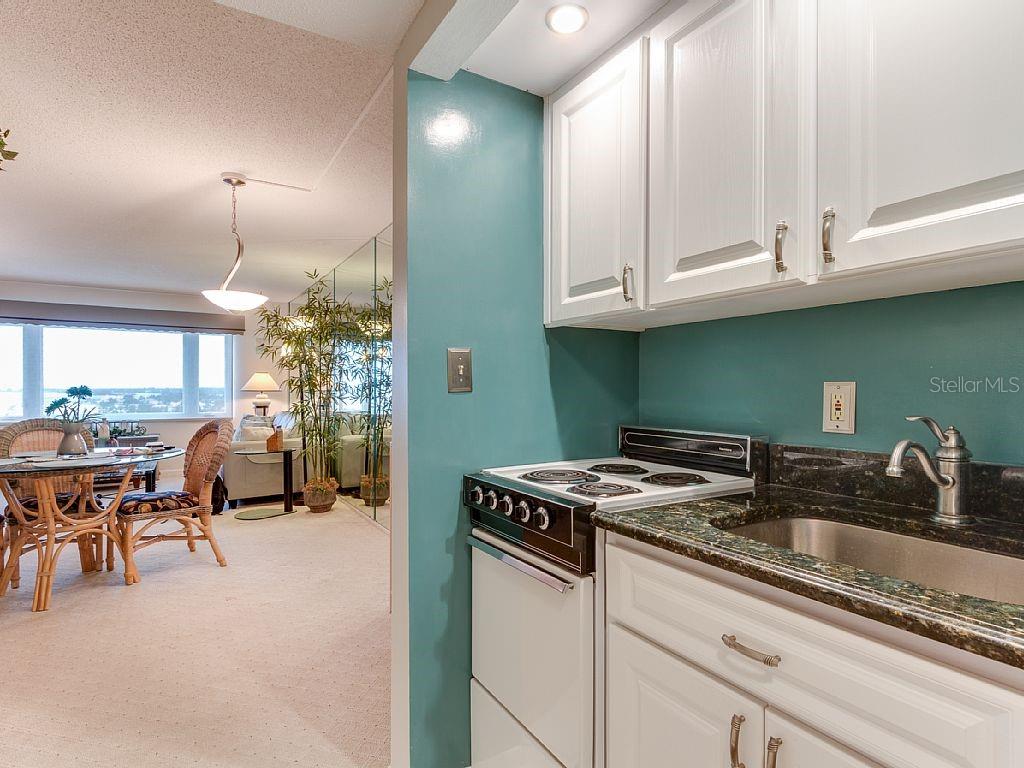 A kitchen with white cabinets and dark countertops opens into a carpeted dining area — 4725 COVE CIRCLE UNIT 906, ST PETERSBURG, FL