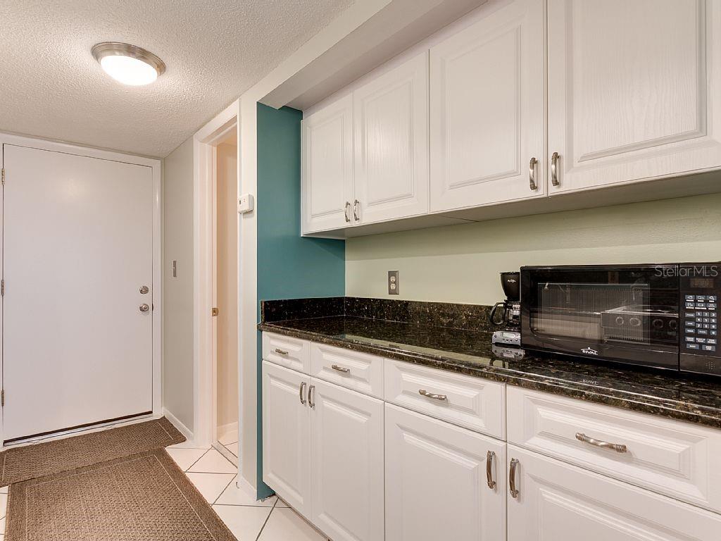 A kitchen features white cabinets, dark granite countertops, and a microwave on the counter — 4725 COVE CIRCLE UNIT 906, ST PETERSBURG, FL