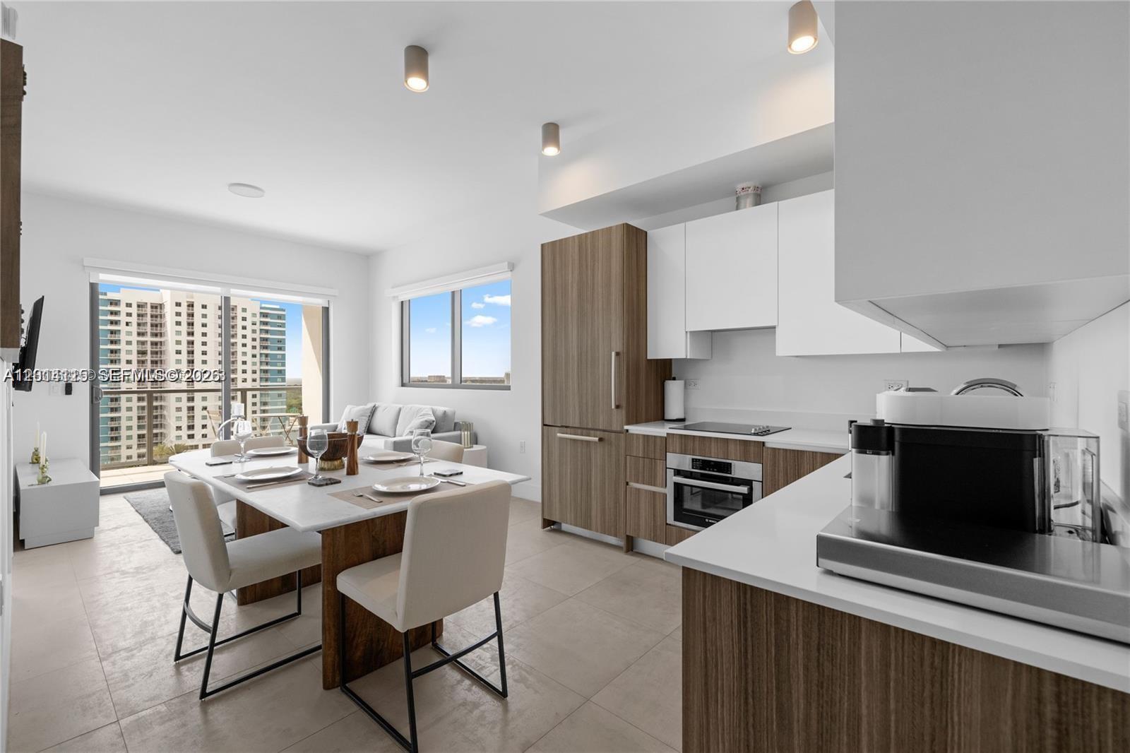 A modern kitchen and dining area features wood-toned cabinetry, white countertops, and a balcony view — 239 SW 9th St # 1502, Miami FL 33130, MIAMI, FL