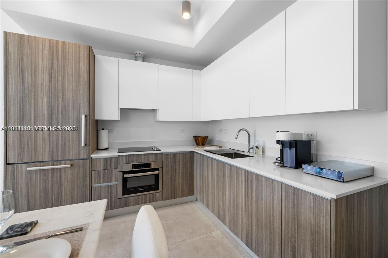 A modern kitchen features white upper cabinets, wood-grain lower cabinets, and white countertops — 239 SW 9th St # 1502, Miami FL 33130, MIAMI, FL