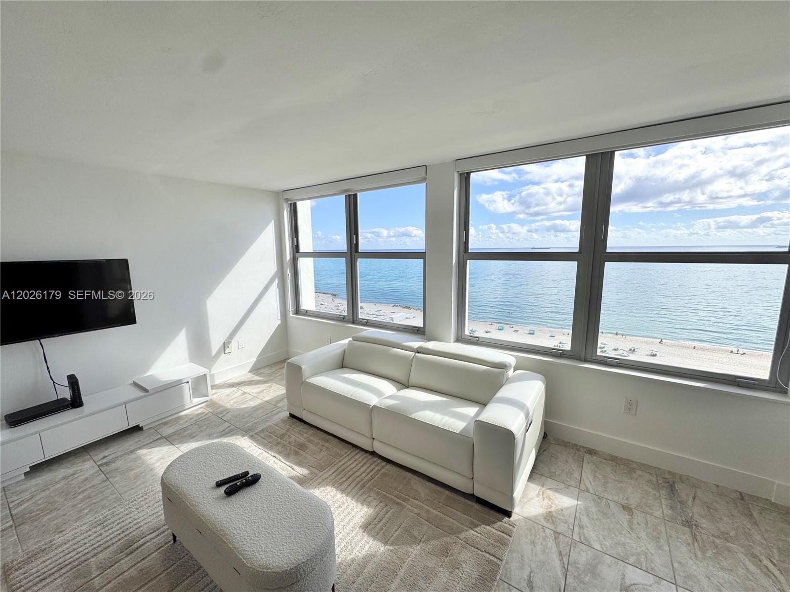 A living room with a white sofa, tiled floors, and large windows overlooking the ocean — 2899 Collins Ave # 1433, Miami Beach FL 33140, MIAMI BEACH, FL