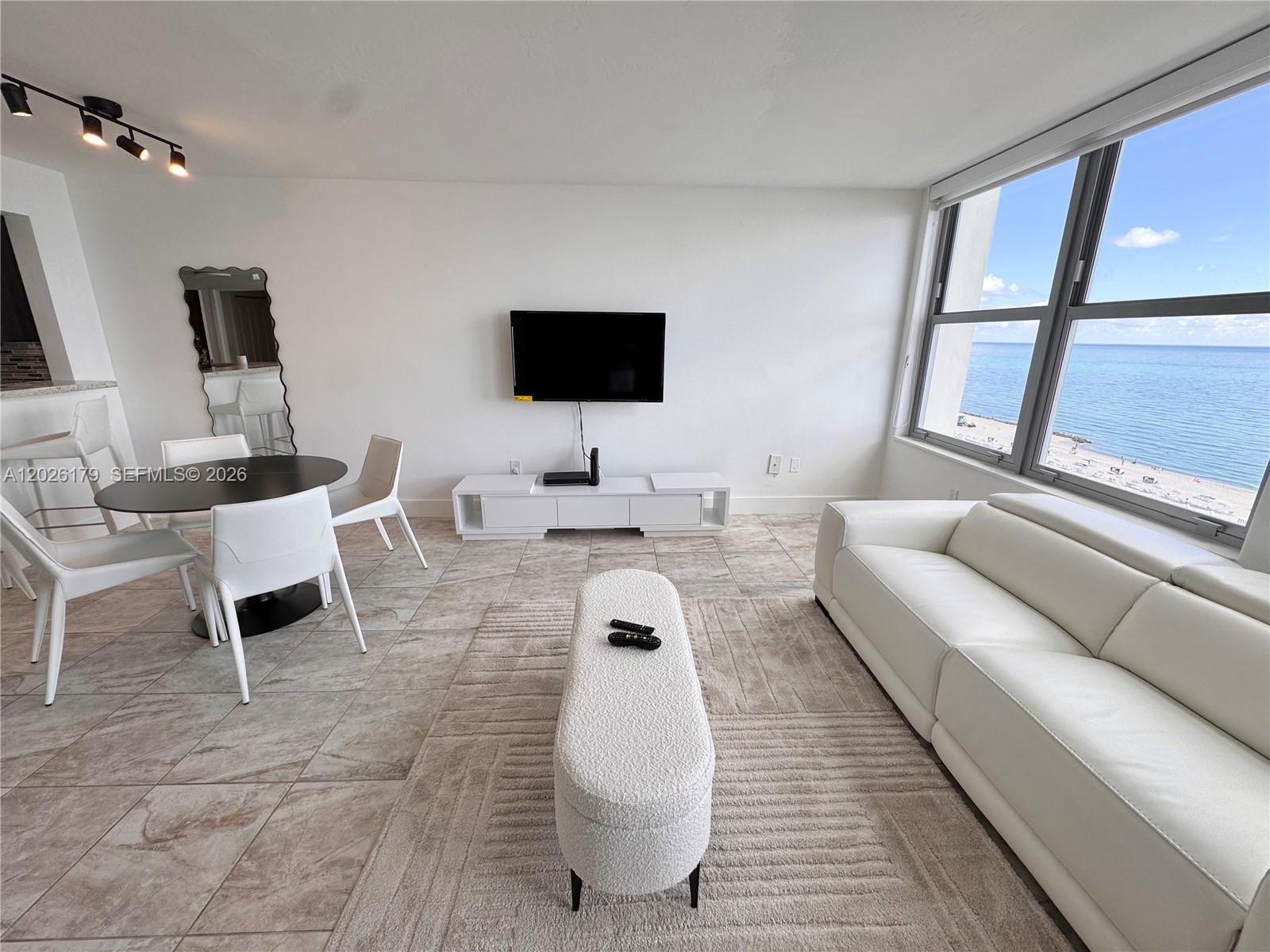 A bright living room features white furniture, a television, and large windows overlooking the ocean — 2899 Collins Ave # 1433, Miami Beach FL 33140, MIAMI BEACH, FL