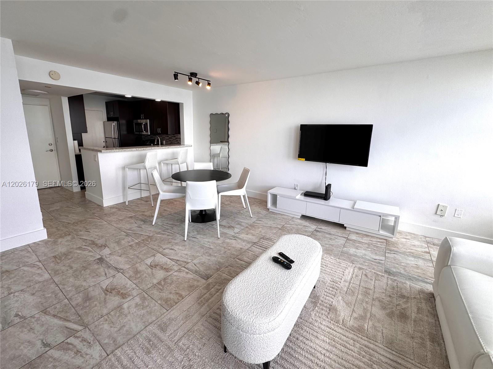 A living room and dining area feature tile floors, white furniture, and an open kitchen — 2899 Collins Ave # 1433, Miami Beach FL 33140, MIAMI BEACH, FL