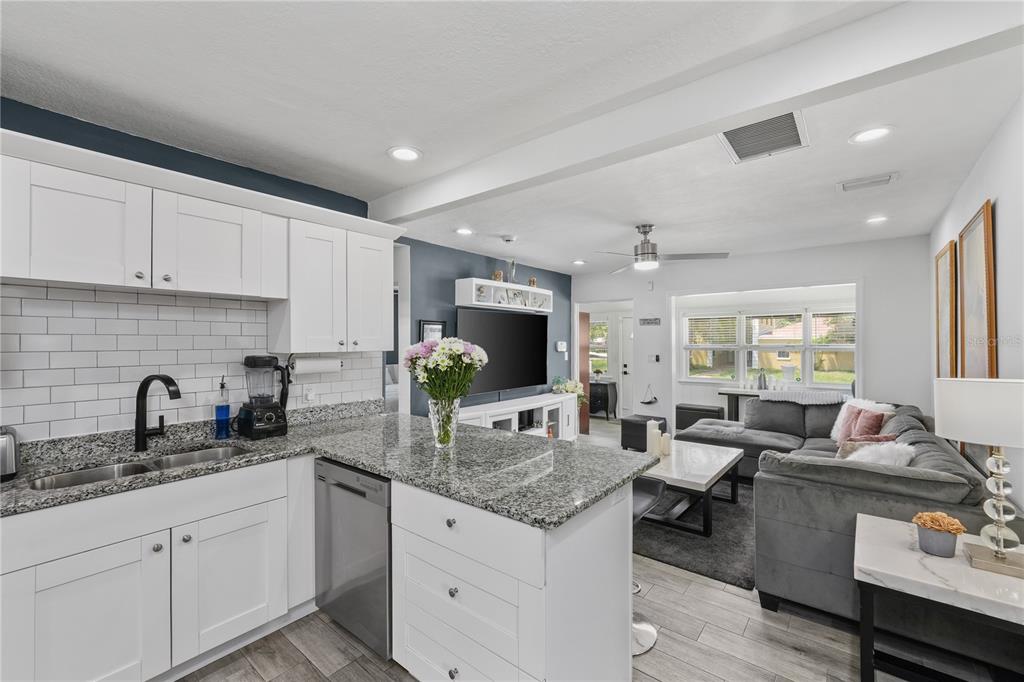 A kitchen with white cabinets and granite countertops opens into a living room with gray furniture — 3260 36TH AVENUE N, ST PETERSBURG, FL