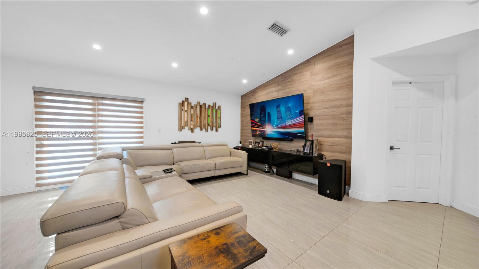 A living room features a beige sectional sofa, a wood-paneled accent wall, and tile flooring — 16898 Crestview Ln, Weston FL 33326, WESTON, FL