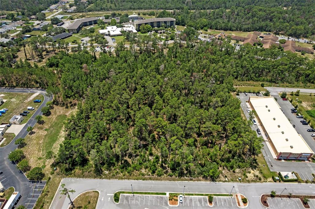 An aerial view shows a wooded lot surrounded by commercial buildings and parking areas — 00 SAGHEER STREET, BROOKSVILLE, FL