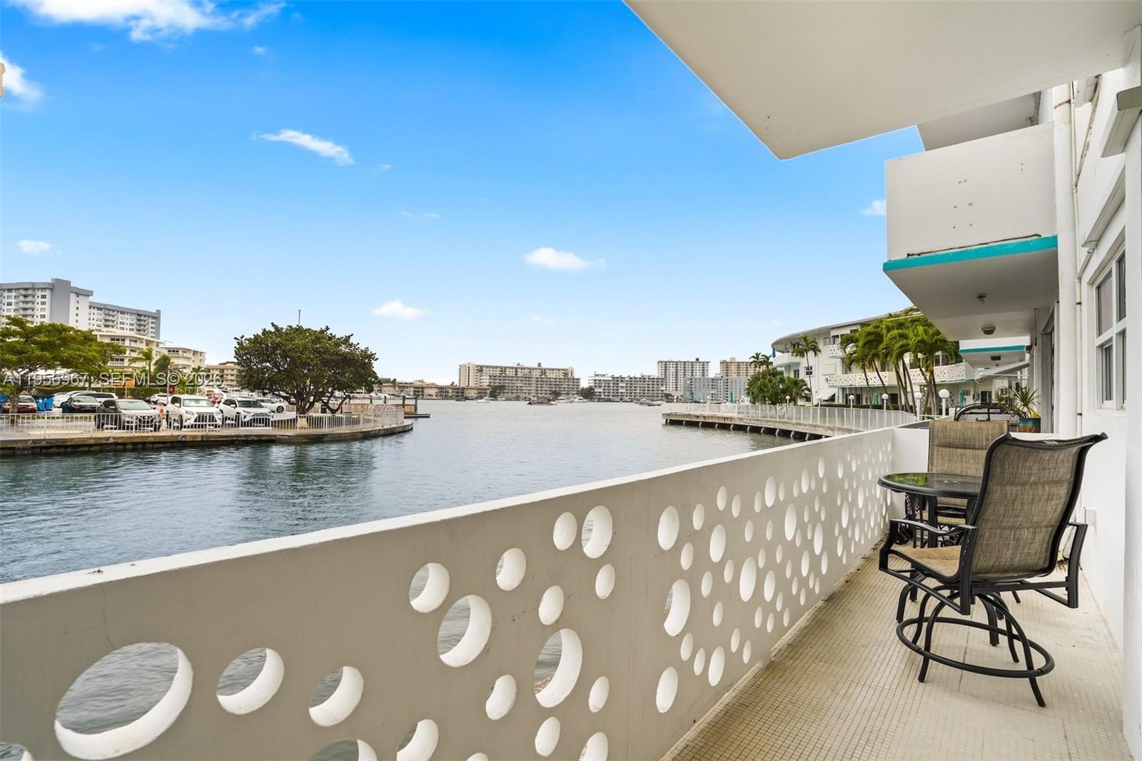 A balcony with a decorative circular-cutout railing overlooks a canal and surrounding apartment buildings — 2500 Diana Dr # 104, Hallandale Beach FL 33009, HALLANDALE BEACH, FL