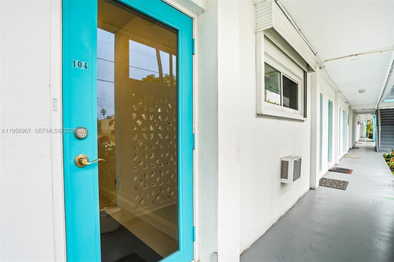 A bright blue door marked 104 opens onto an exterior walkway with white walls — 2500 Diana Dr # 104, Hallandale Beach FL 33009, HALLANDALE BEACH, FL
