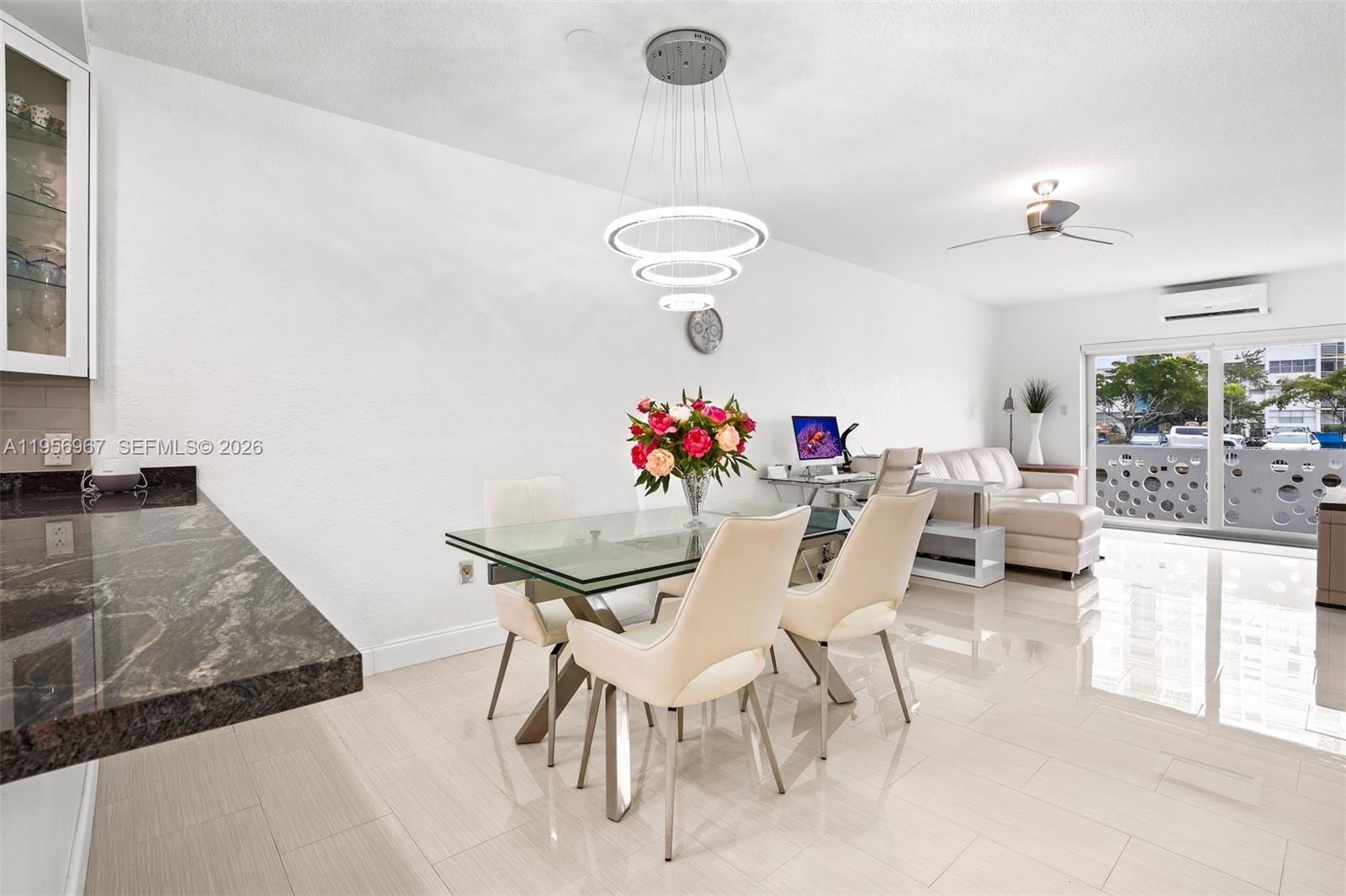 A dining area with a glass table, modern chandelier, and adjacent living space with balcony — 2500 Diana Dr # 104, Hallandale Beach FL 33009, HALLANDALE BEACH, FL
