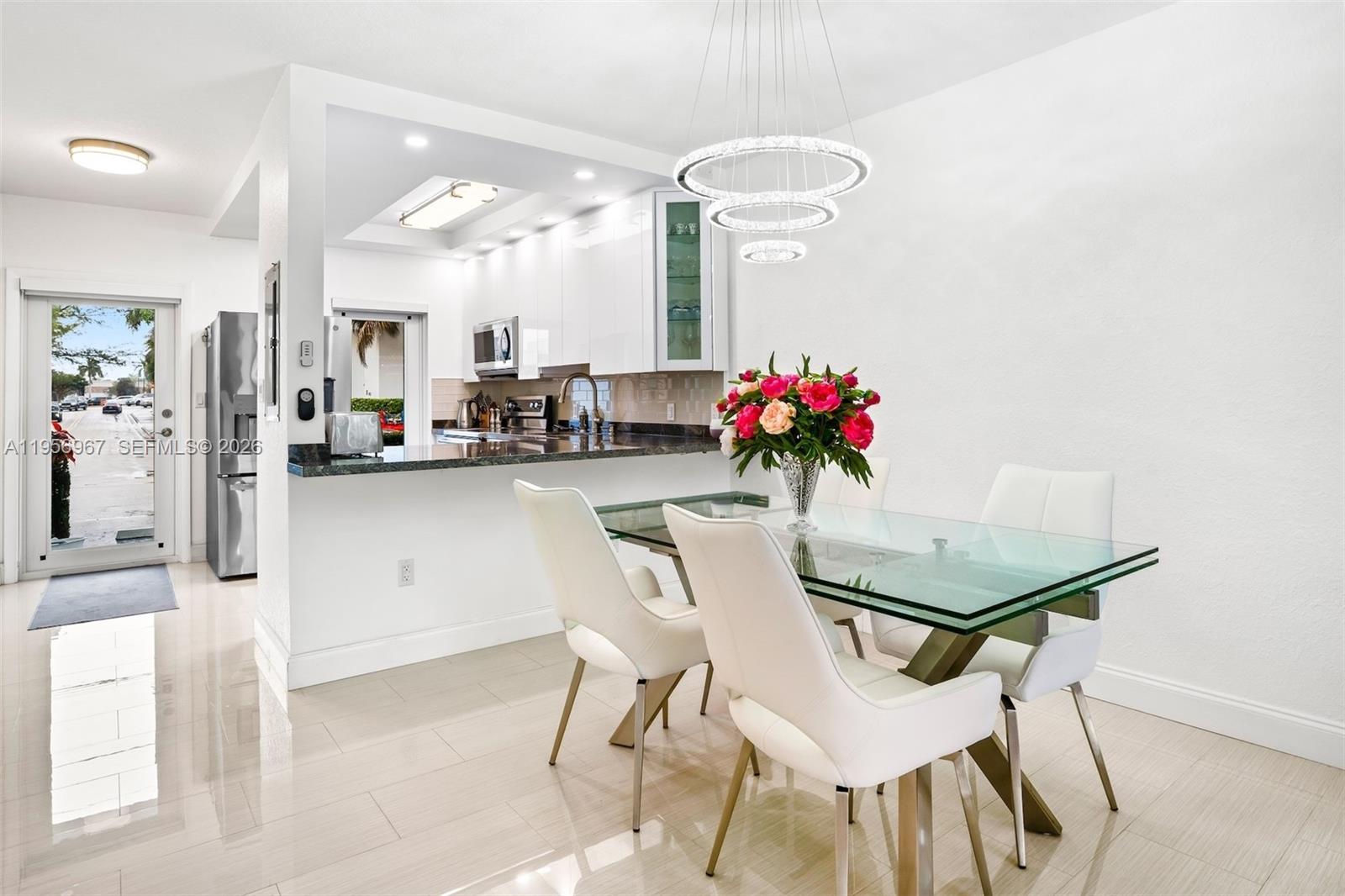 A dining area with a glass table and white chairs sits beside a modern kitchen — 2500 Diana Dr # 104, Hallandale Beach FL 33009, HALLANDALE BEACH, FL