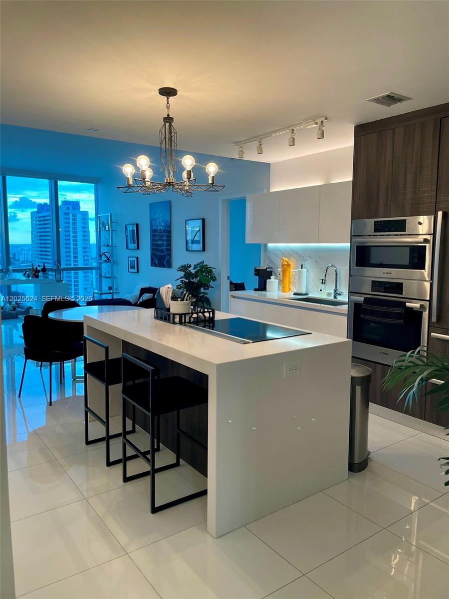 A modern kitchen features a white waterfall island, dark cabinetry, and a contemporary chandelier — 851 NE 1st Ave # 1808, Miami FL 33132, MIAMI, FL