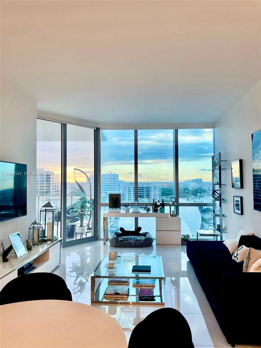 A modern living room features floor-to-ceiling windows with city views and a dark sofa — 851 NE 1st Ave # 1808, Miami FL 33132, MIAMI, FL