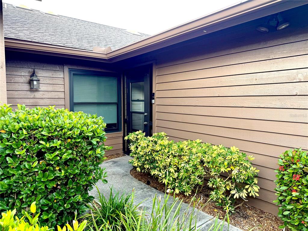 An open screen door reveals a tiled entryway leading to a white front door — 5813 MERION WAY UNIT 5813, SARASOTA, FL