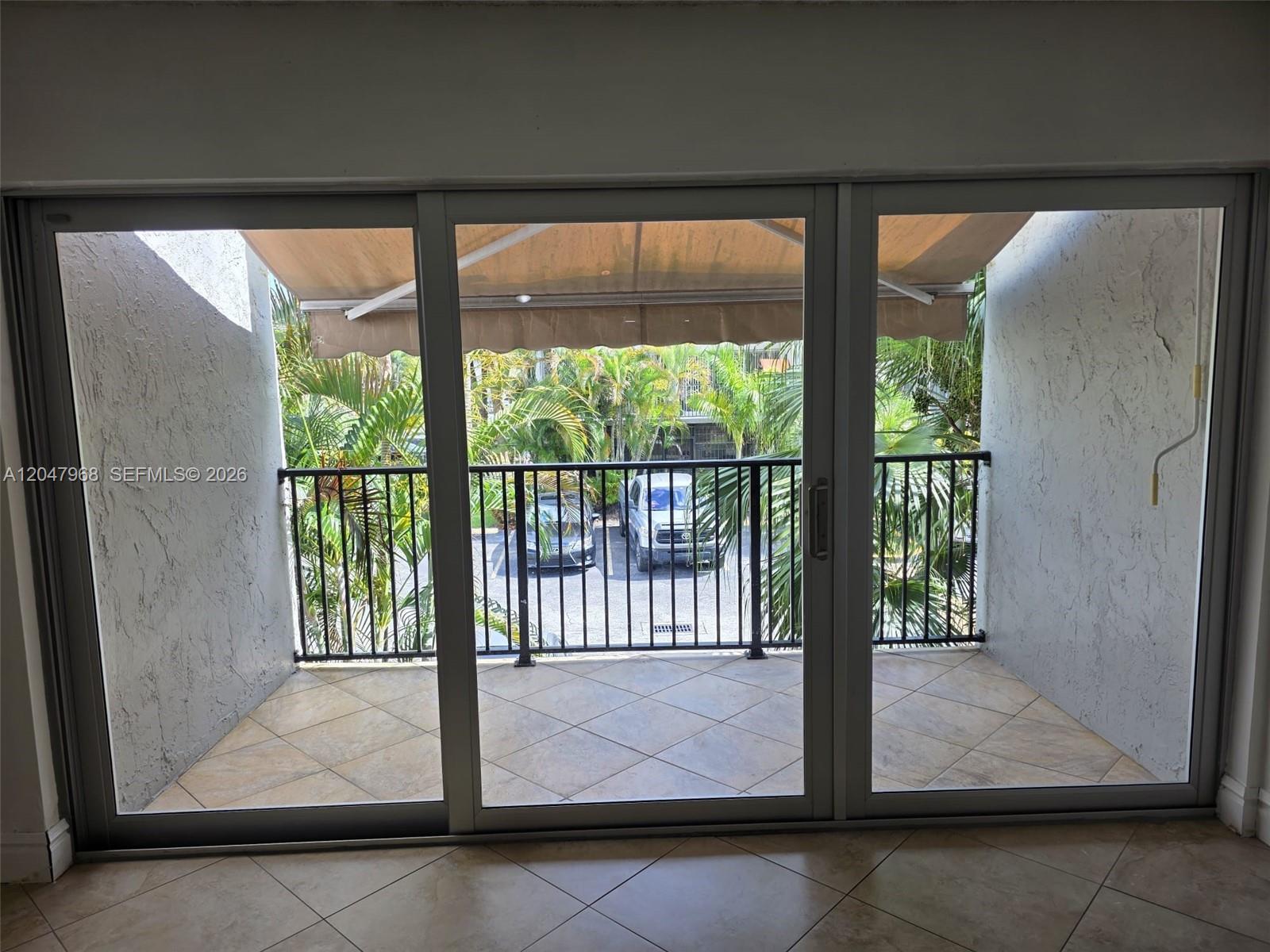 A balcony with tiled flooring and a metal railing is viewed through large sliding glass doors — 40 NW 87th Ave # D201, Miami FL 33172, MIAMI, FL