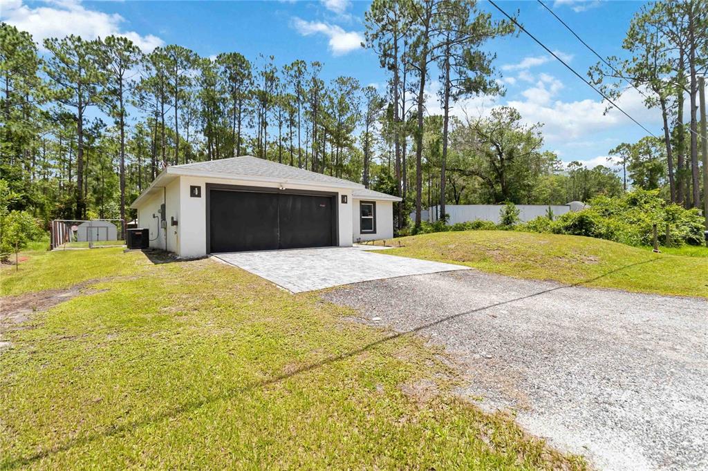 A detached garage with a dark door, a paved apron, and a gravel driveway — 1639 11TH AVENUE, DELAND, FL