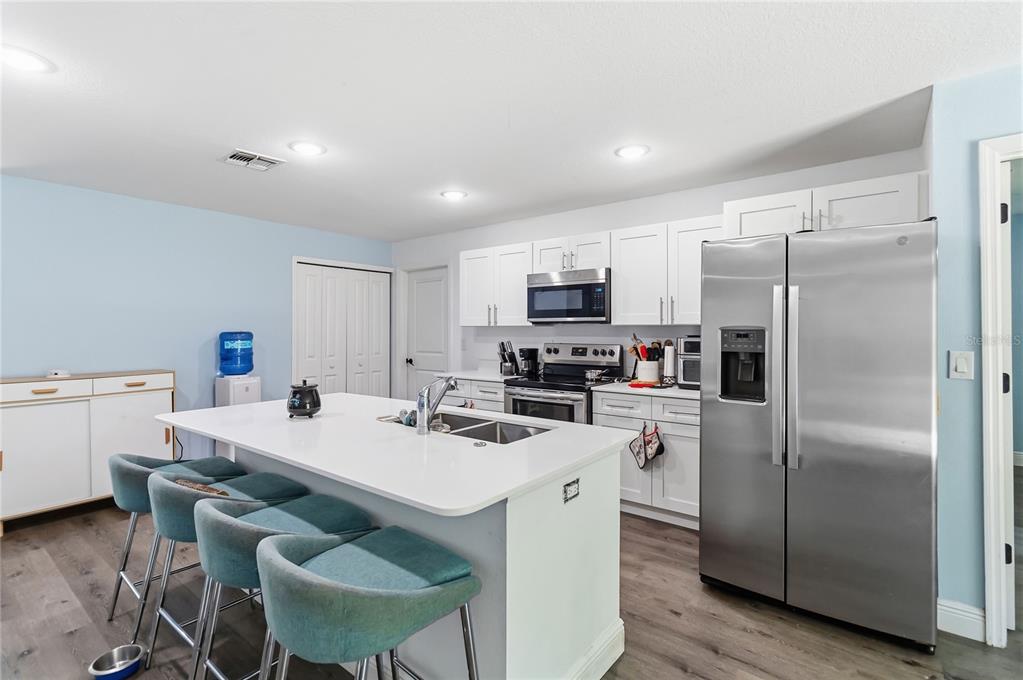A kitchen features a white island with teal stools, stainless steel appliances, and white cabinetry — 1639 11TH AVENUE, DELAND, FL